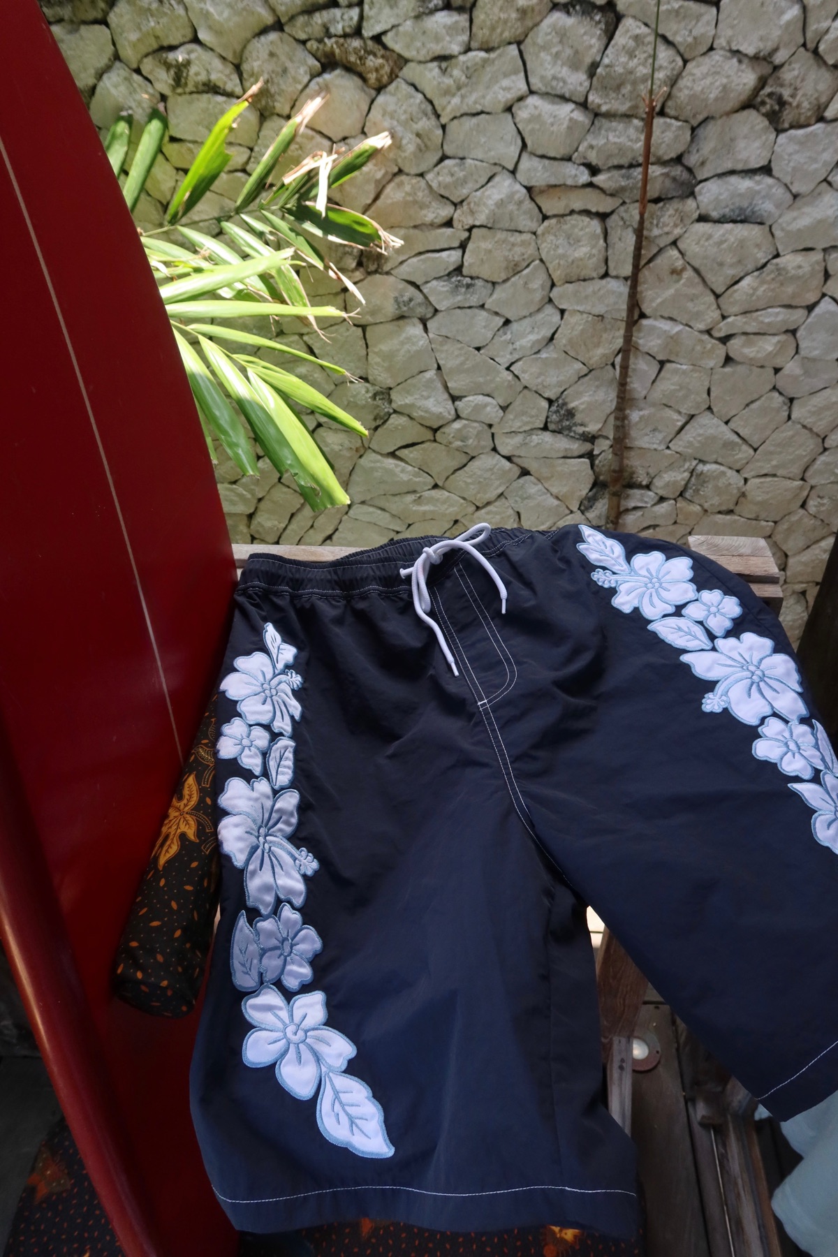 Navy board shorts with hibiscus applique worn on the beach