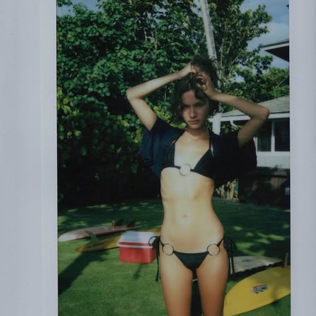 A Polaroid photograph of a girl on the grass beside two surfboards